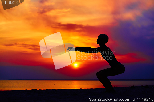 Image of Silhouette of woman standing at yoga pose on the beach during an amazing sunset