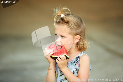 Image of Adorable blonde girl eats a slice of watermelon outdoors.