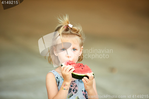 Image of Adorable blonde girl eats a slice of watermelon outdoors.