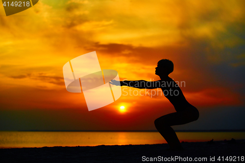 Image of Silhouette of woman standing at yoga pose on the beach during an amazing sunset