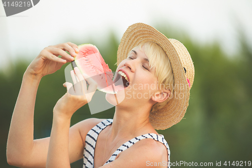 Image of Beautiful girl in straw hat eating fresh watermelon. Film camera style