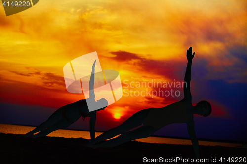 Image of Yoga people training and meditating in warrior pose outside by beach at sunrise or sunset.