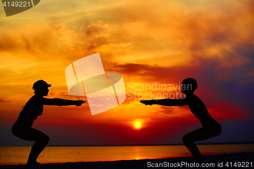 Image of Yoga people training and meditating in warrior pose outside by beach at sunrise or sunset.