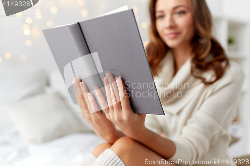 Image of happy young woman reading book in bed at home