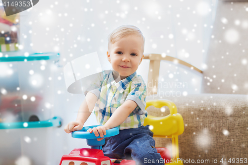 Image of happy little baby boy driving ride-on car at home