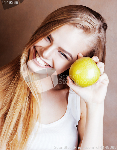Image of young pretty blond woman with green apple happy cheerful smiling close up on warm brown background, lifestyle people concept