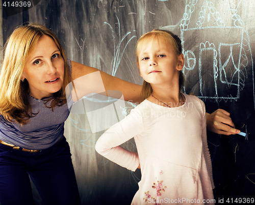 Image of portrait of mature woman teacher with little cute blonde girl pupil writing on blackboard together, lifestyle people concept