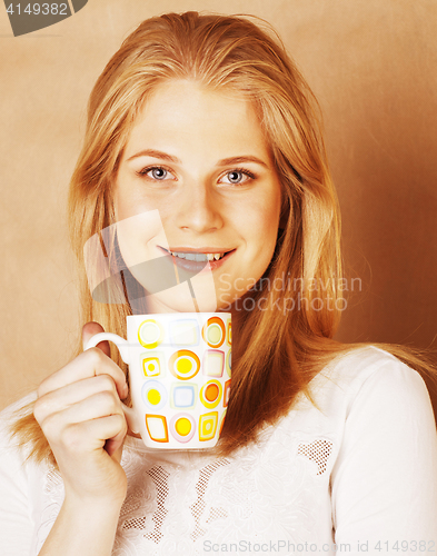 Image of young cute blond girl drinking coffee close up on warm brown bac