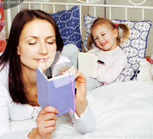 Image of portrait of mother and daughter laying in bed  reading and writi