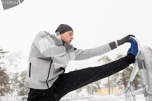 Image of sports man stretching leg at fence in winter