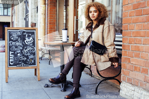 Image of young pretty african american women drinking coffee outside in c