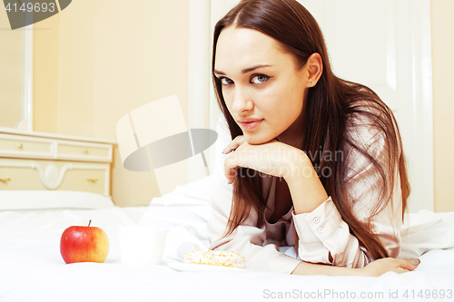 Image of young pretty brunette woman laying in bed, luxury white interior