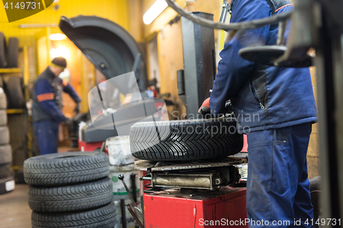 Image of Professional auto mechanic replacing tire on wheel in car repair service.