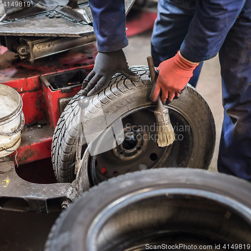 Image of Professional auto mechanic replacing tire on wheel in car repair service.
