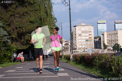 Image of young smiling multiethnic couple jogging in the city