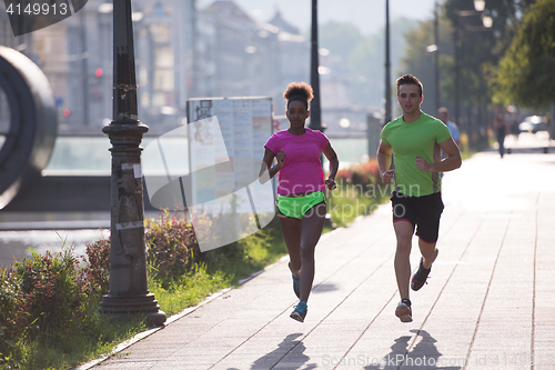 Image of young smiling multiethnic couple jogging in the city