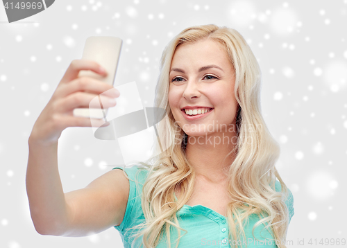 Image of smiling young woman taking selfie with smartphone