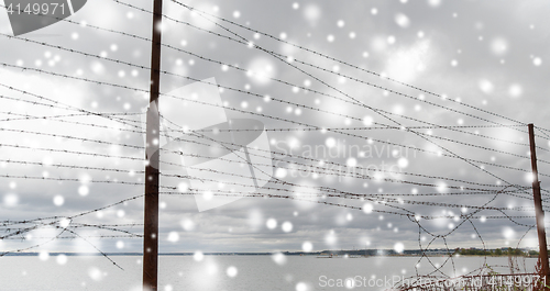 Image of broken barb wire fence over gray sky and sea