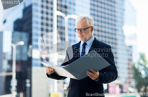 Image of senior businessman with ring binder folder in city