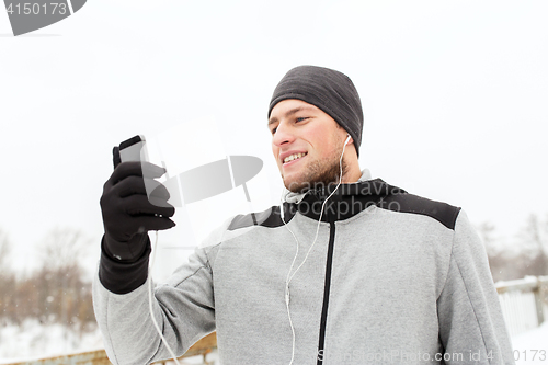 Image of happy man with earphones and smartphone in winter