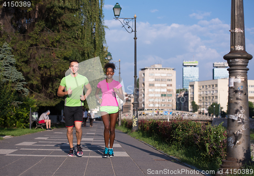 Image of young smiling multiethnic couple jogging in the city