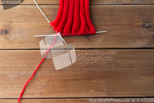 Image of hand-knitted item with knitting needles on wood
