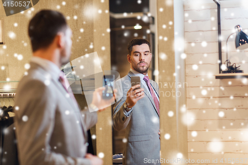 Image of man in suit taking mirror selfie at clothing store