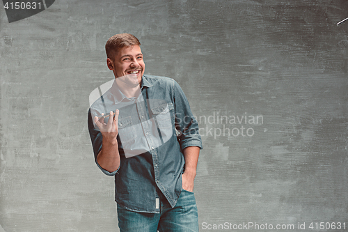 Image of The young smiling caucasian businessman on gray background with phone