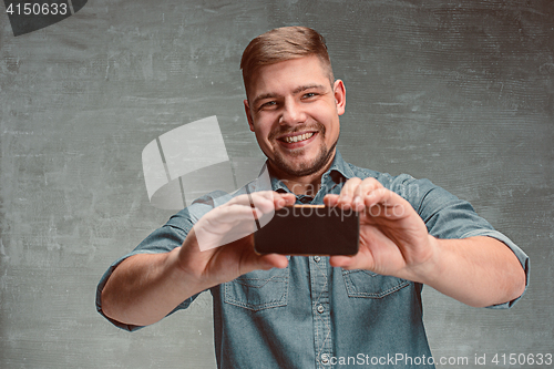 Image of The young smiling caucasian businessman on gray background with phone