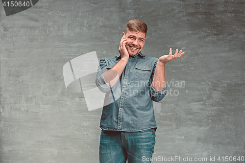 Image of The young smiling caucasian businessman on gray background talking with phone