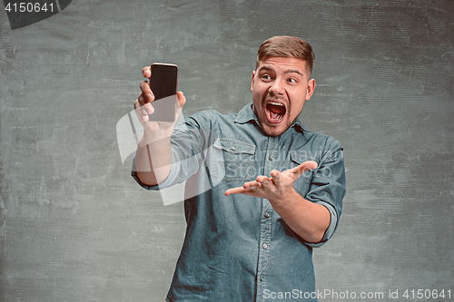 Image of The young smiling caucasian businessman on gray background with phone