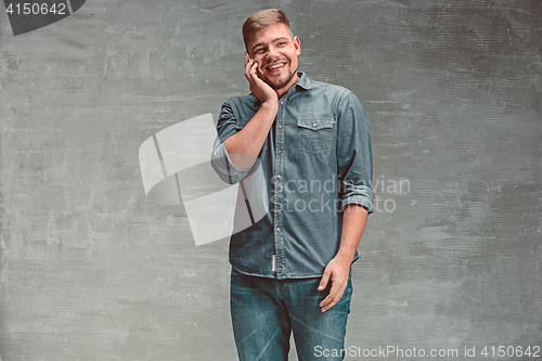 Image of The young smiling caucasian businessman on gray background talking with phone