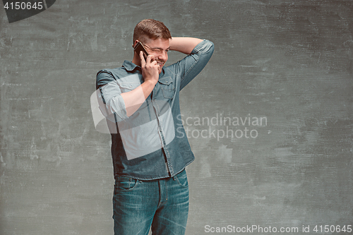 Image of The young smiling caucasian businessman on gray background talking with phone