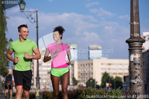 Image of young smiling multiethnic couple jogging in the city