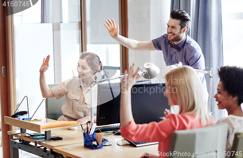 Image of happy creative team waving hands in office