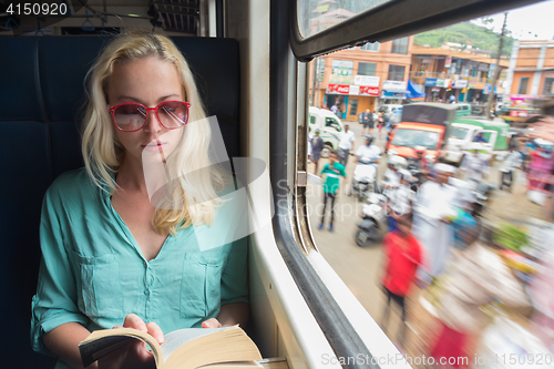 Image of Blonde caucasian woman reading book on train by the window.