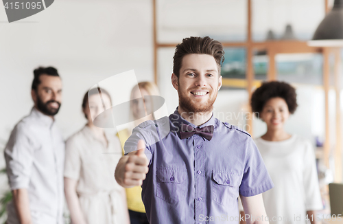 Image of happy man showing thumbs up over team in office