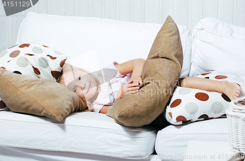 Image of little cute blonde norwegian girl playing on sofa with pillows, lifestyle people concept