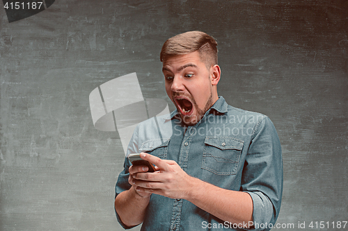 Image of The young smiling caucasian businessman on gray background with phone