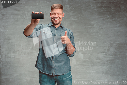 Image of The young smiling caucasian businessman on gray background with phone