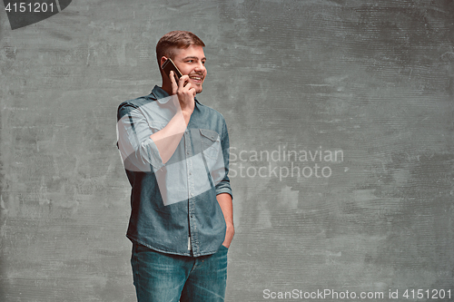 Image of The young smiling caucasian businessman on gray background talking with phone