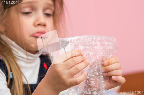 Image of Upset girl pouting cheeks eats bubbles packaging film