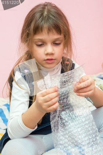 Image of Five-year girl sitting on the bed and eats bubbles packaging package