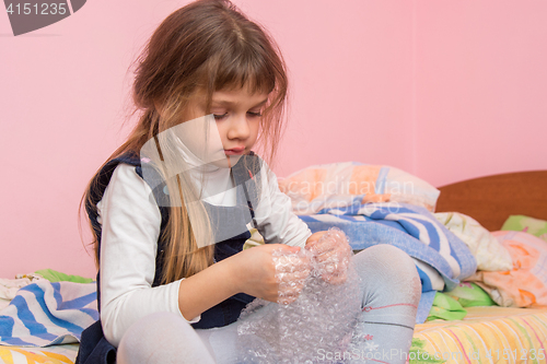 Image of Sad girl sitting on the bed and eats bubbles on the packaging film