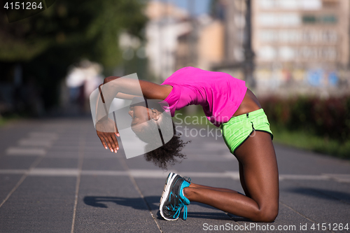 Image of sporty young african american woman stretching outdoors