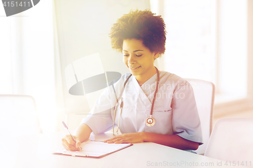 Image of happy female doctor or nurse writing to clipboard