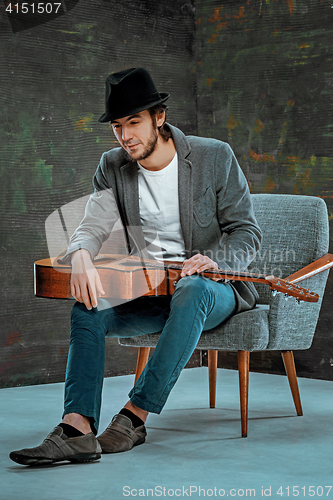 Image of Cool guy sitting with guitar on gray background