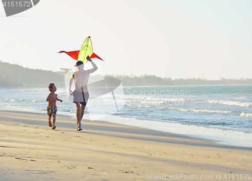 Image of father with son, sunset at the seacoast playing kite, happy family 