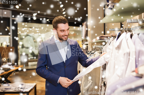 Image of happy young man choosing clothes in clothing store