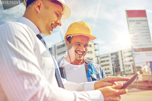 Image of happy builders in hardhats with tablet pc outdoors